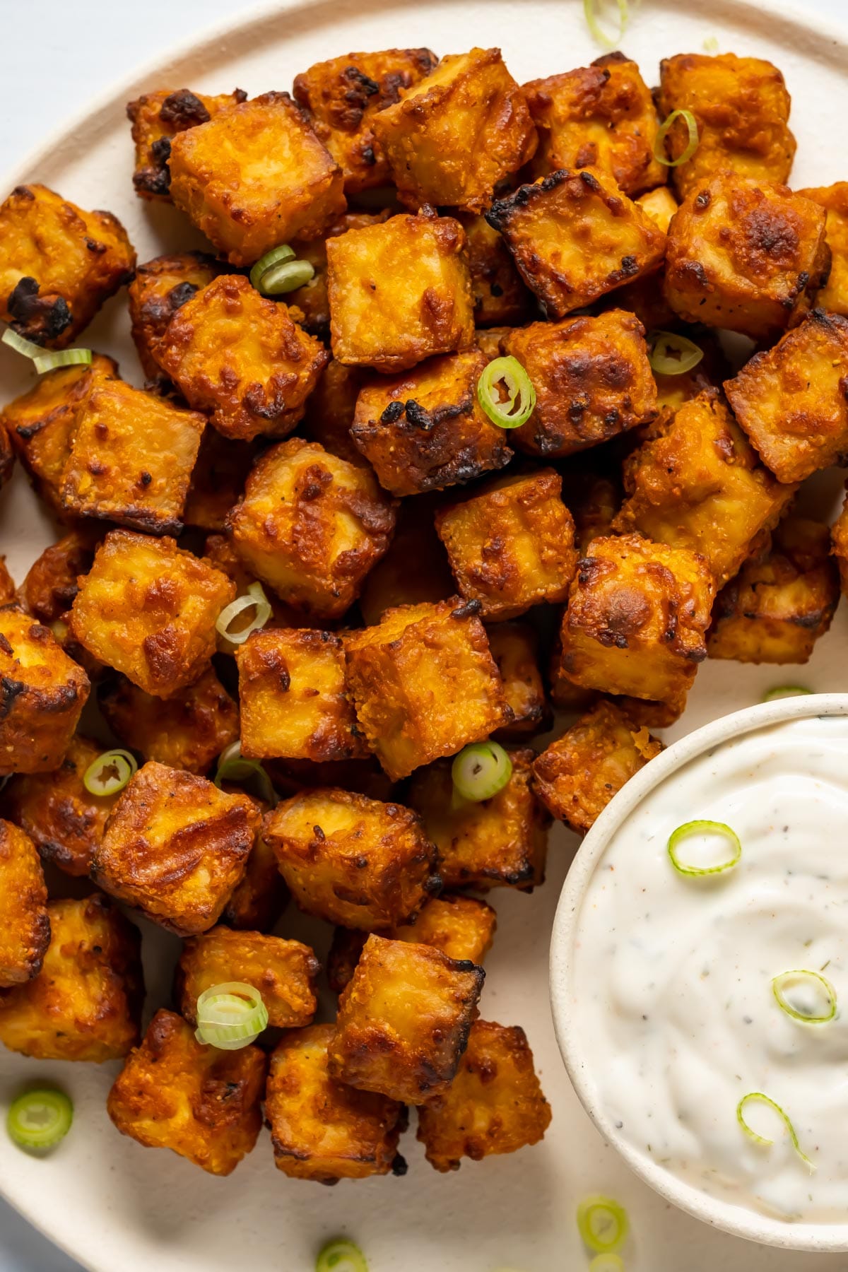 Air fryer tofu with chopped green onions and ranch dressing on a white plate.