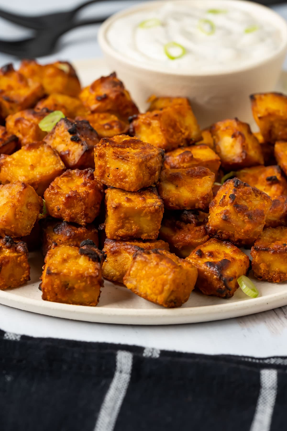 Air fryer tofu with ranch dressing and chopped green onions on a white plate.