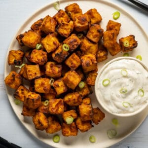 Air fryer tofu on a white plate with chopped green onions and vegan ranch dressing.