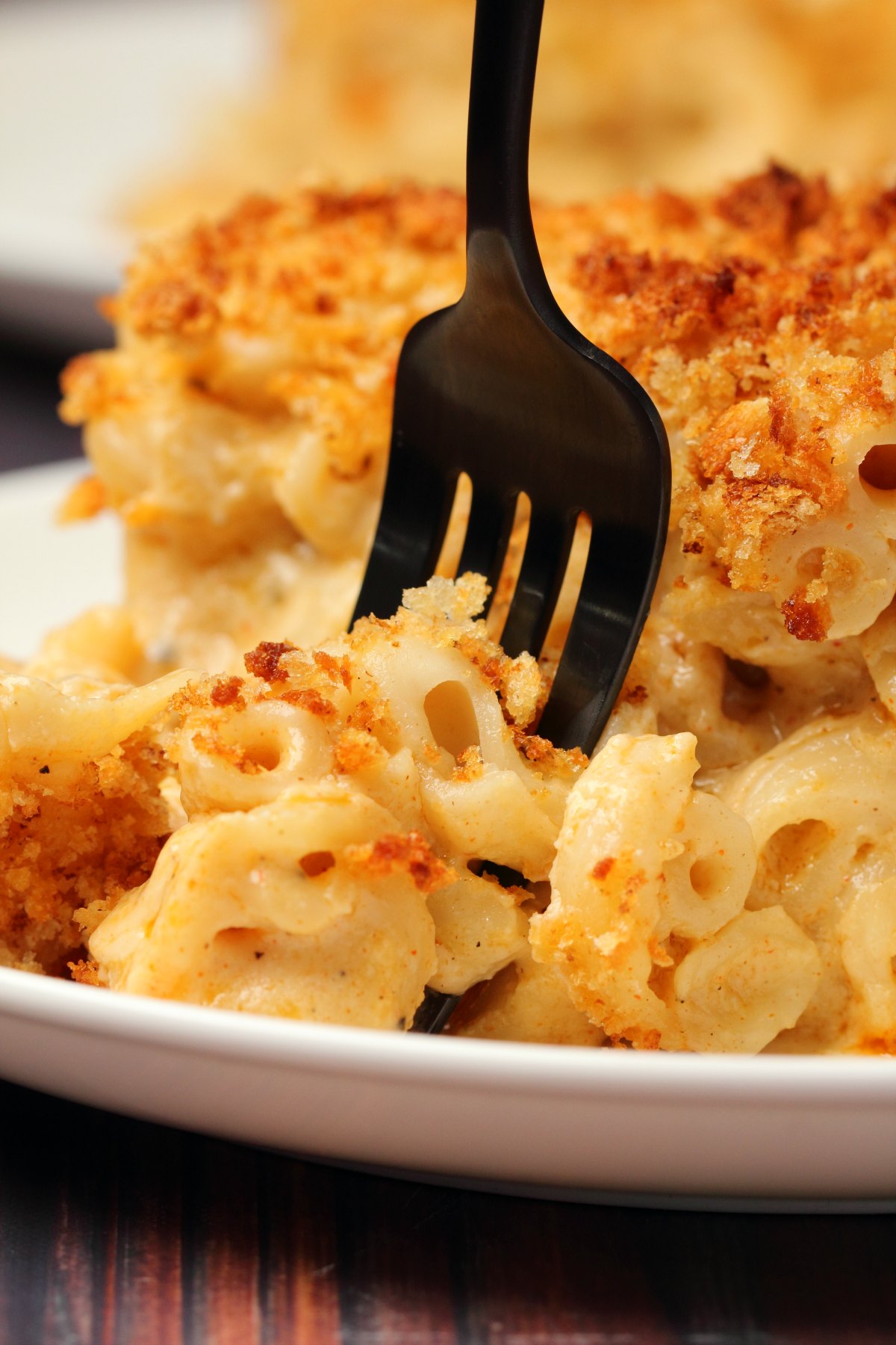 A slice of baked vegan mac and cheese on a white plate with a fork. 