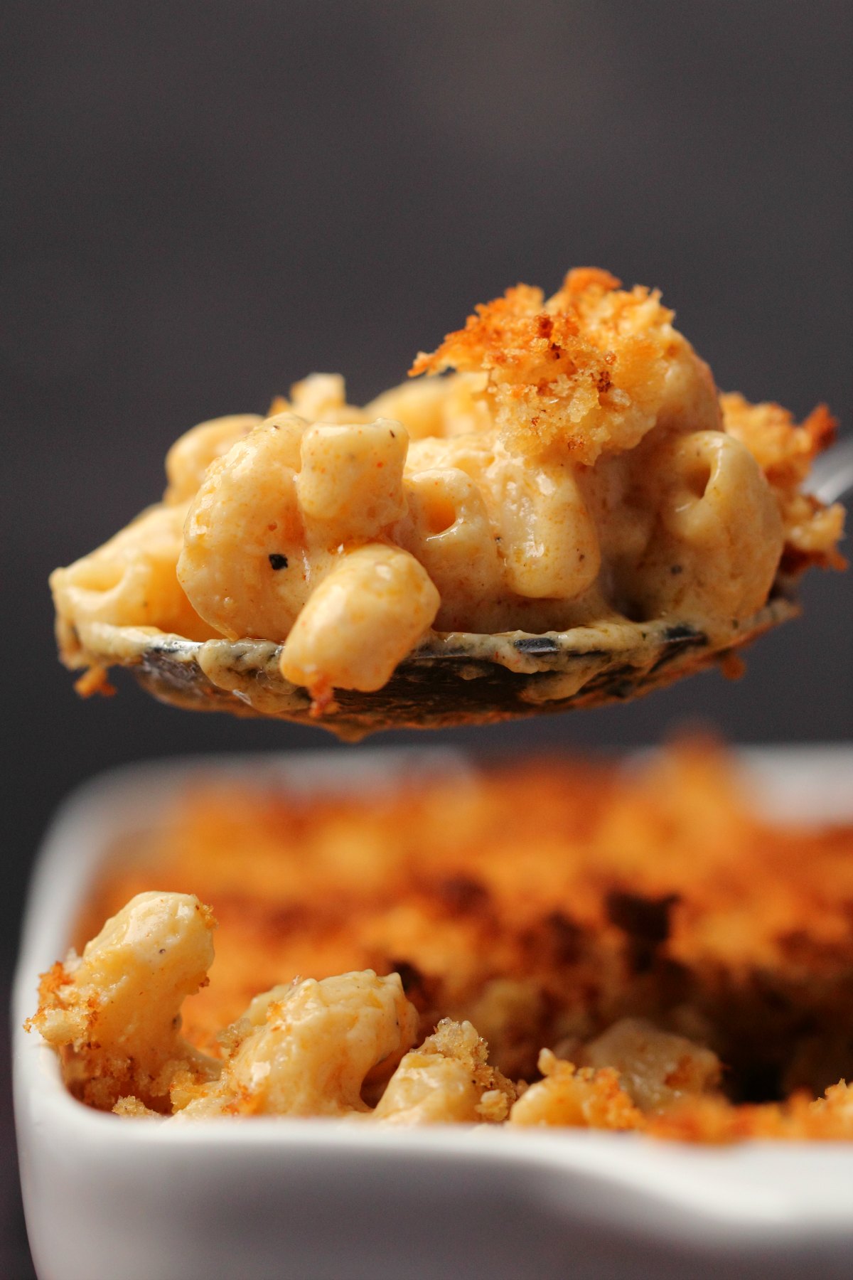 A large spoonful of vegan mac and cheese lifting out of a white dish. 