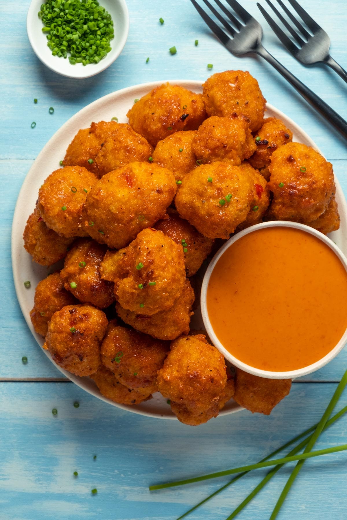 Bang bang cauliflower on a plate with chopped chives and bang bang sauce.