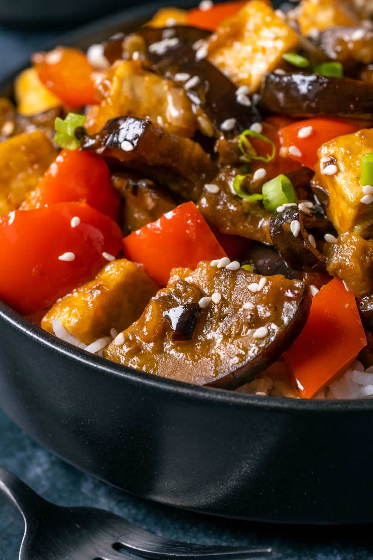 Eggplant tofu stir fry with rice in a black bowl.