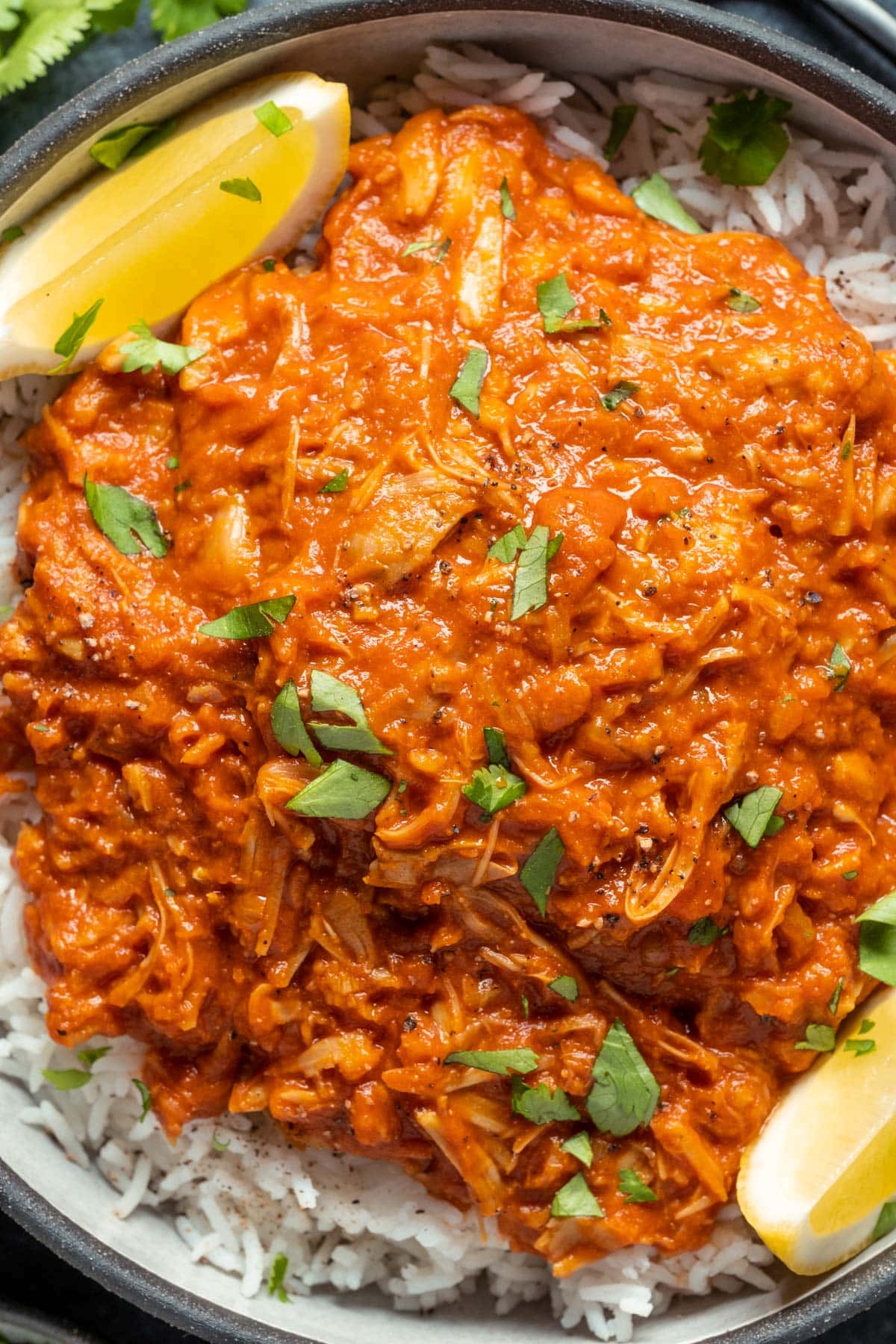 Jackfruit curry with rice and lemon wedges in a black bowl.