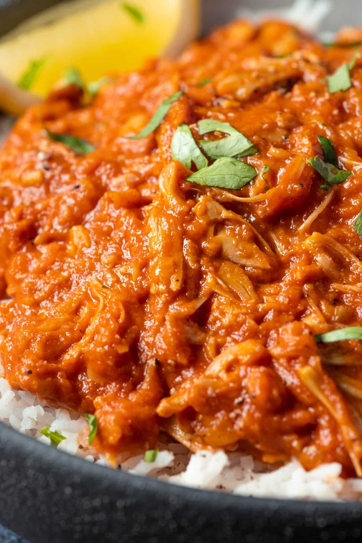 Jackfruit curry with rice and lemon wedges in a black bowl.