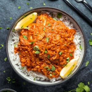 Jackfruit curry with rice and lemon wedges in a black bowl.