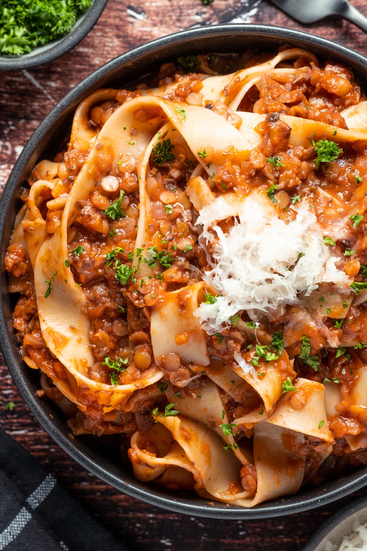 Lentil ragu with vegan parmesan and fresh chopped parsley in a black bowl. 