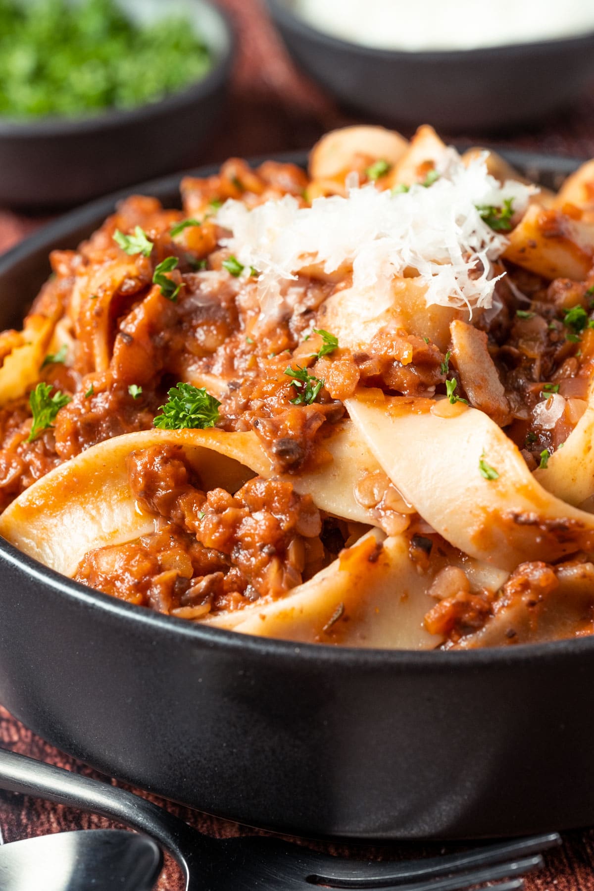 Lentil ragu with vegan parmesan and fresh chopped parsley in a black bowl.