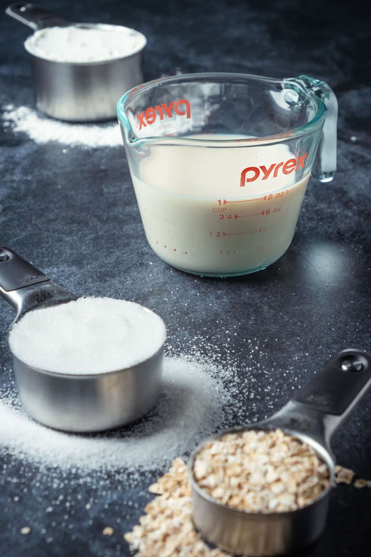 Flour, soy milk, sugar and oats in measuring cups.