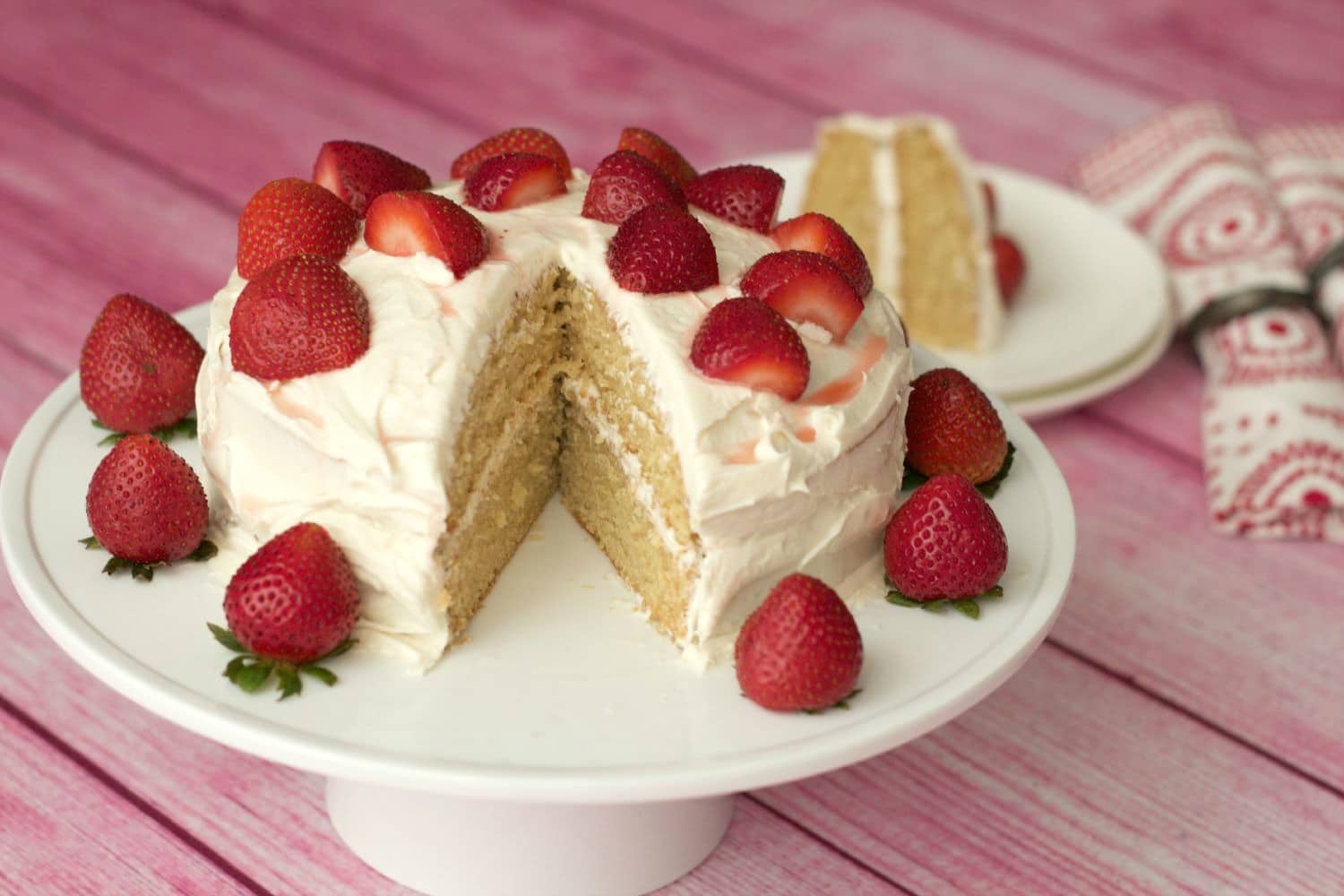 Vegan vanilla cake topped with fresh strawberries on a white cake stand. 