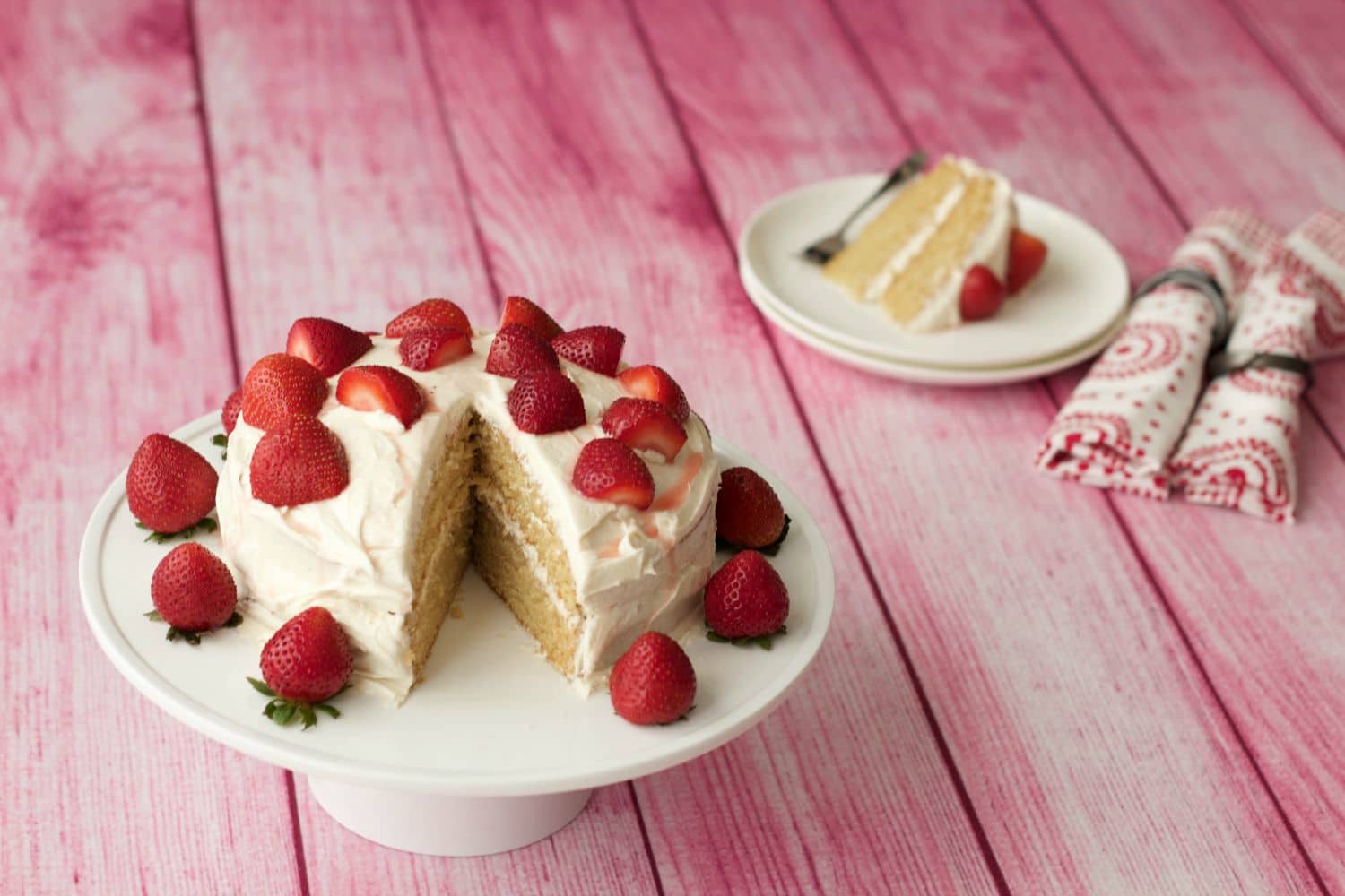 Vegan vanilla cake topped with fresh strawberries on a white cake stand. 