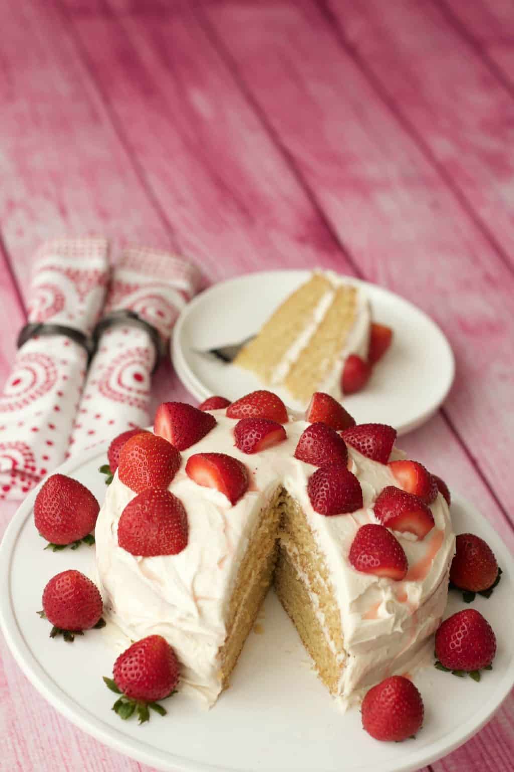 Vegan vanilla cake topped with fresh strawberries on a white cake stand. 