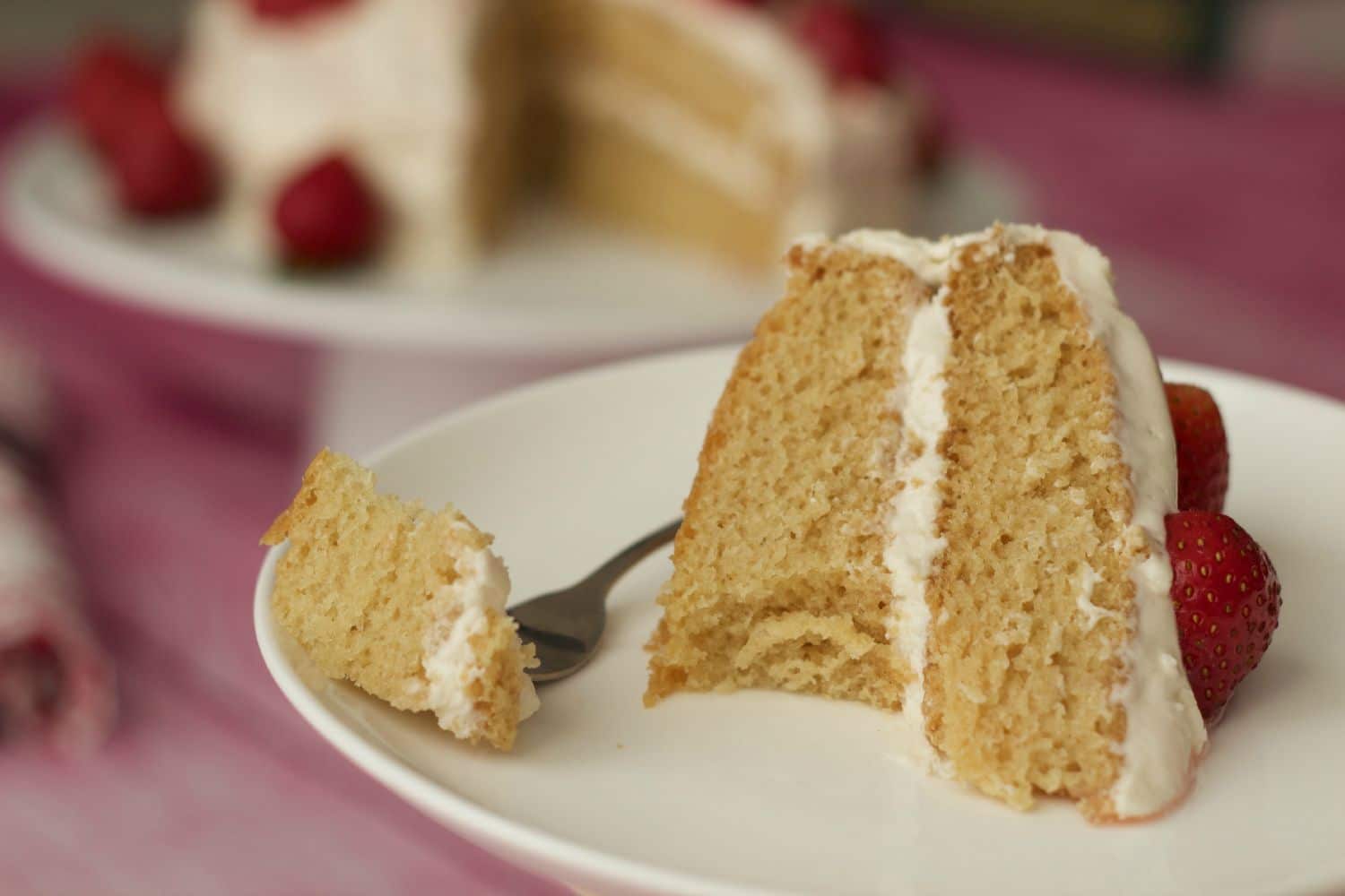 A slice of vegan vanilla cake on a white plate with a cake fork. 