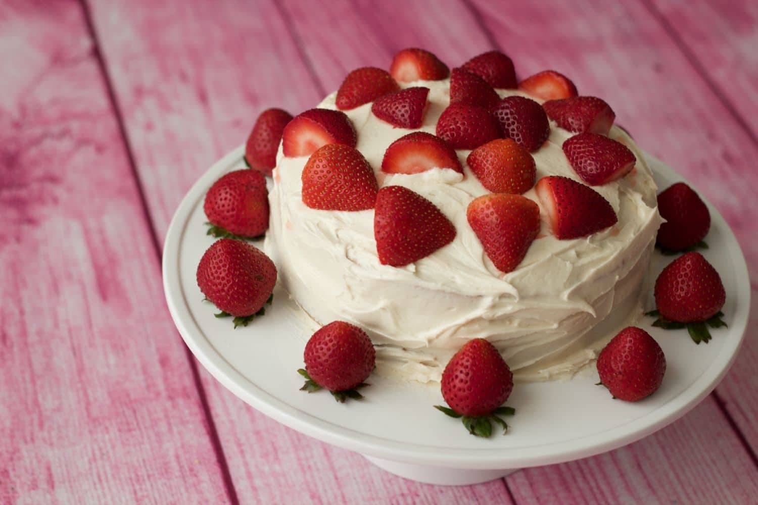 Vegan vanilla cake topped with fresh strawberries on a white cake stand. 