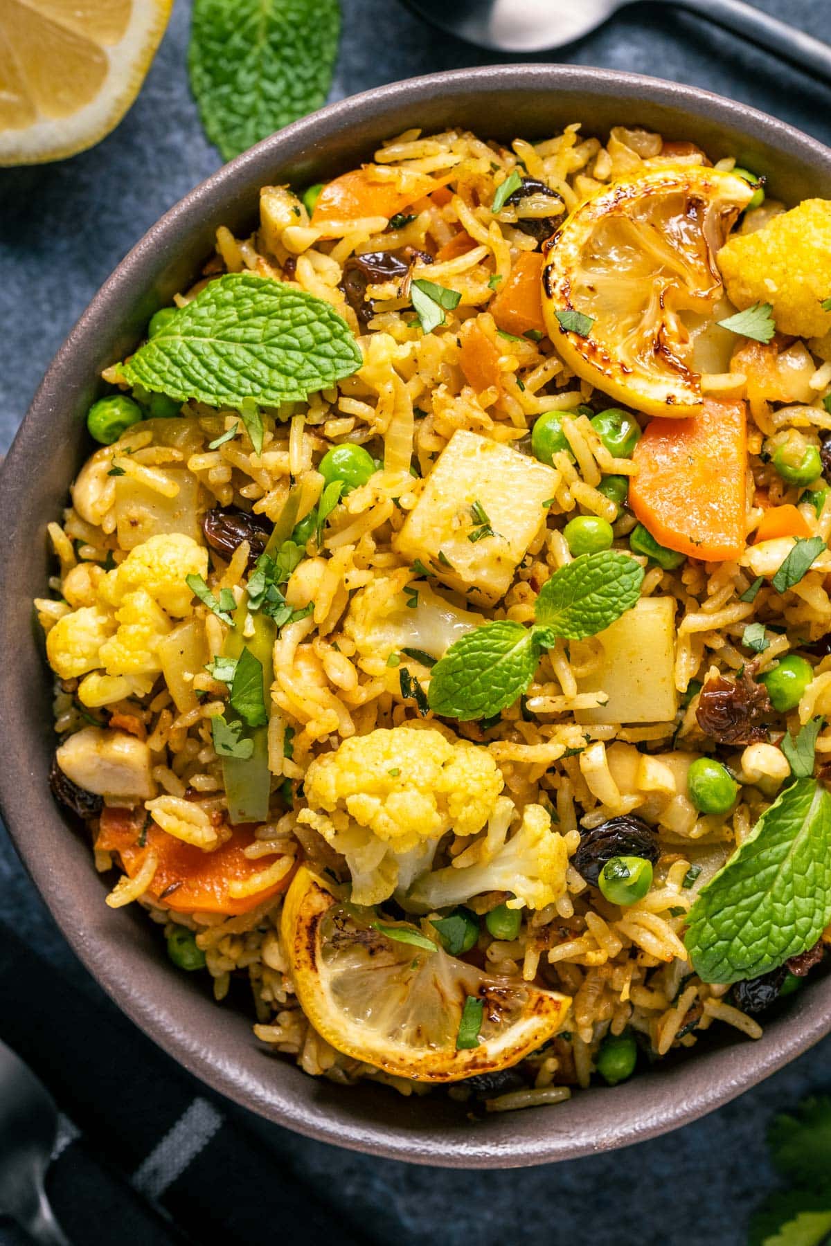 Bowl of vegan biryani topped with fresh mint leaves, chopped cilantro and charred lemon slices. 