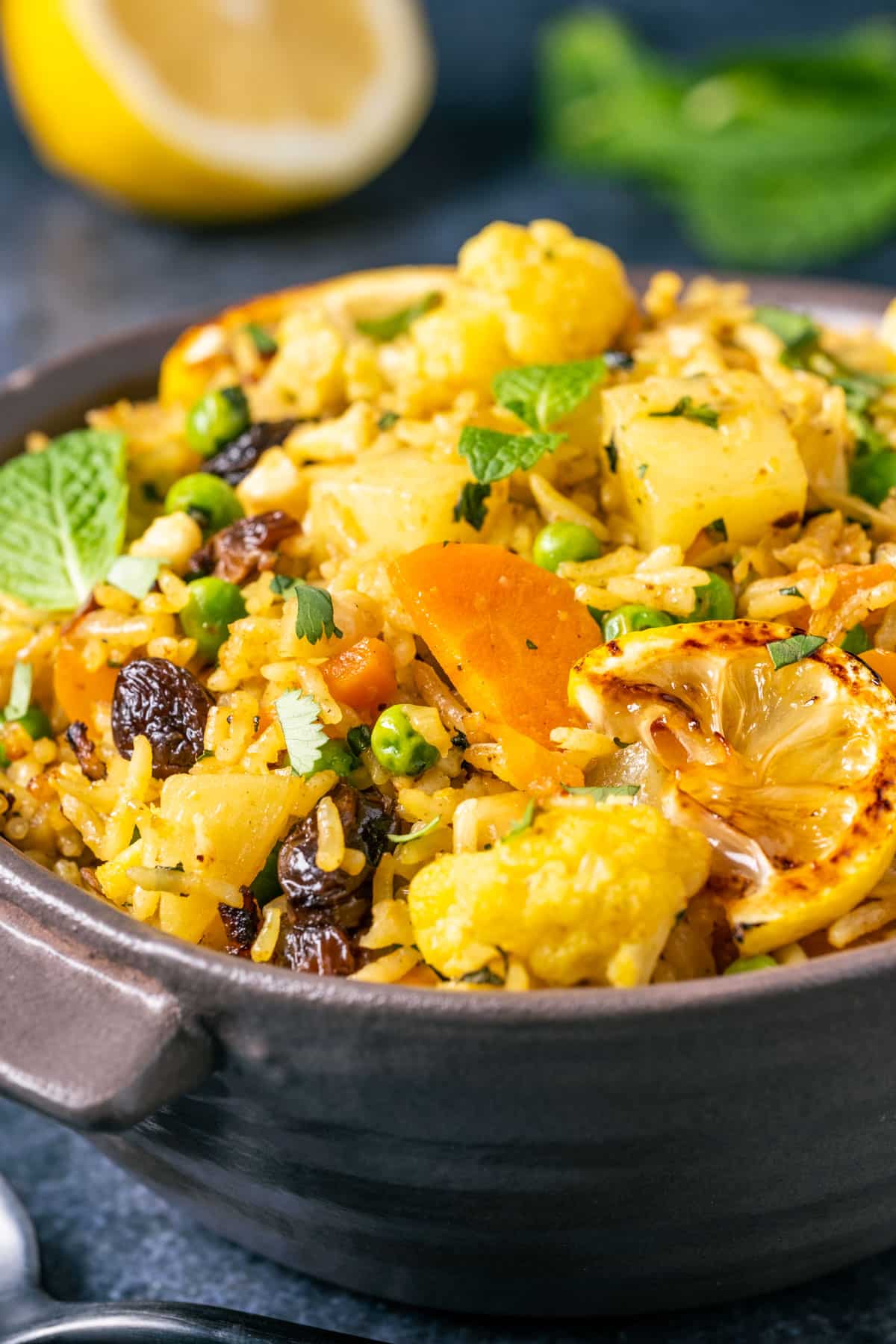 Bowl of vegan biryani topped with fresh mint leaves, chopped cilantro and charred lemon slices.