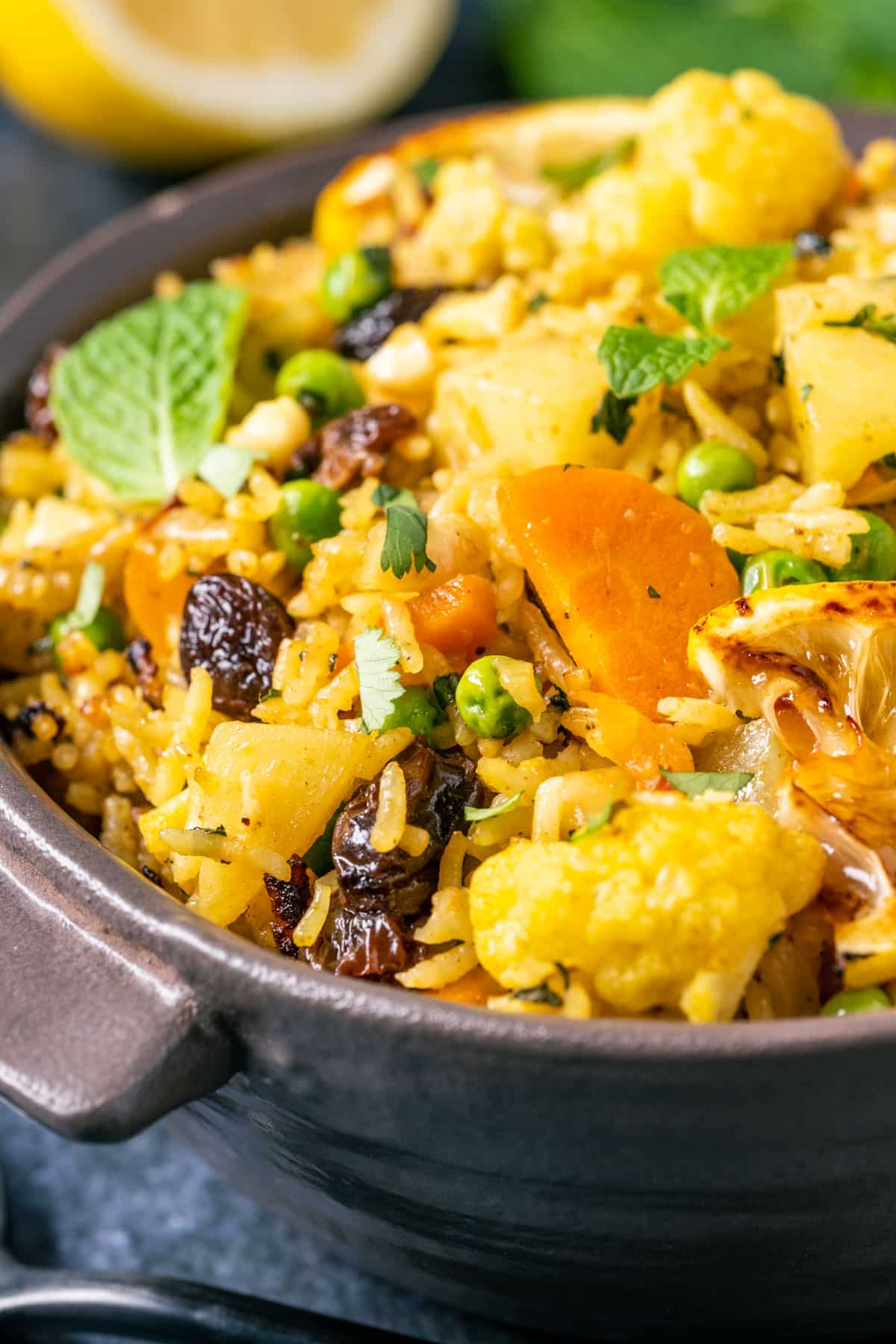 Bowl of vegan biryani topped with fresh mint leaves, chopped cilantro and charred lemon slices.