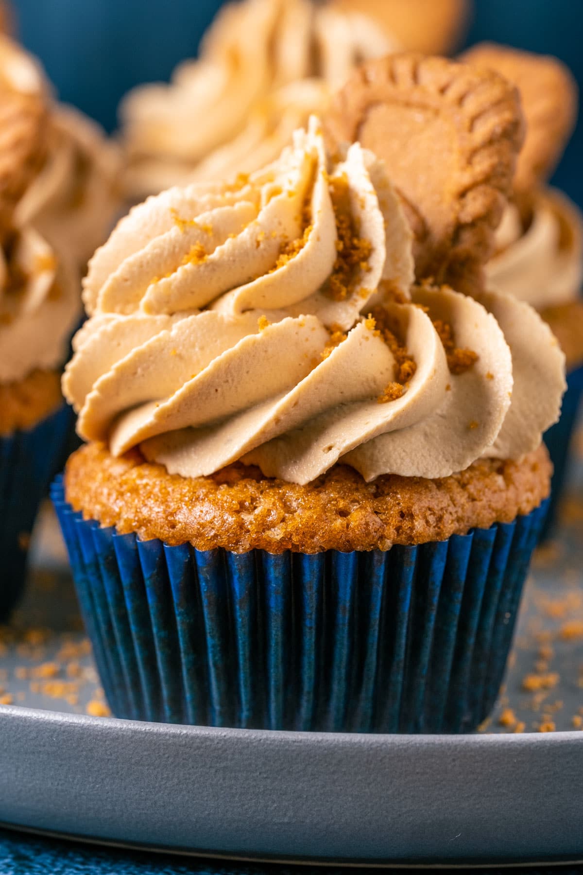 Vegan biscoff cupcakes topped with frosting and biscoff cookies on a gray plate. 