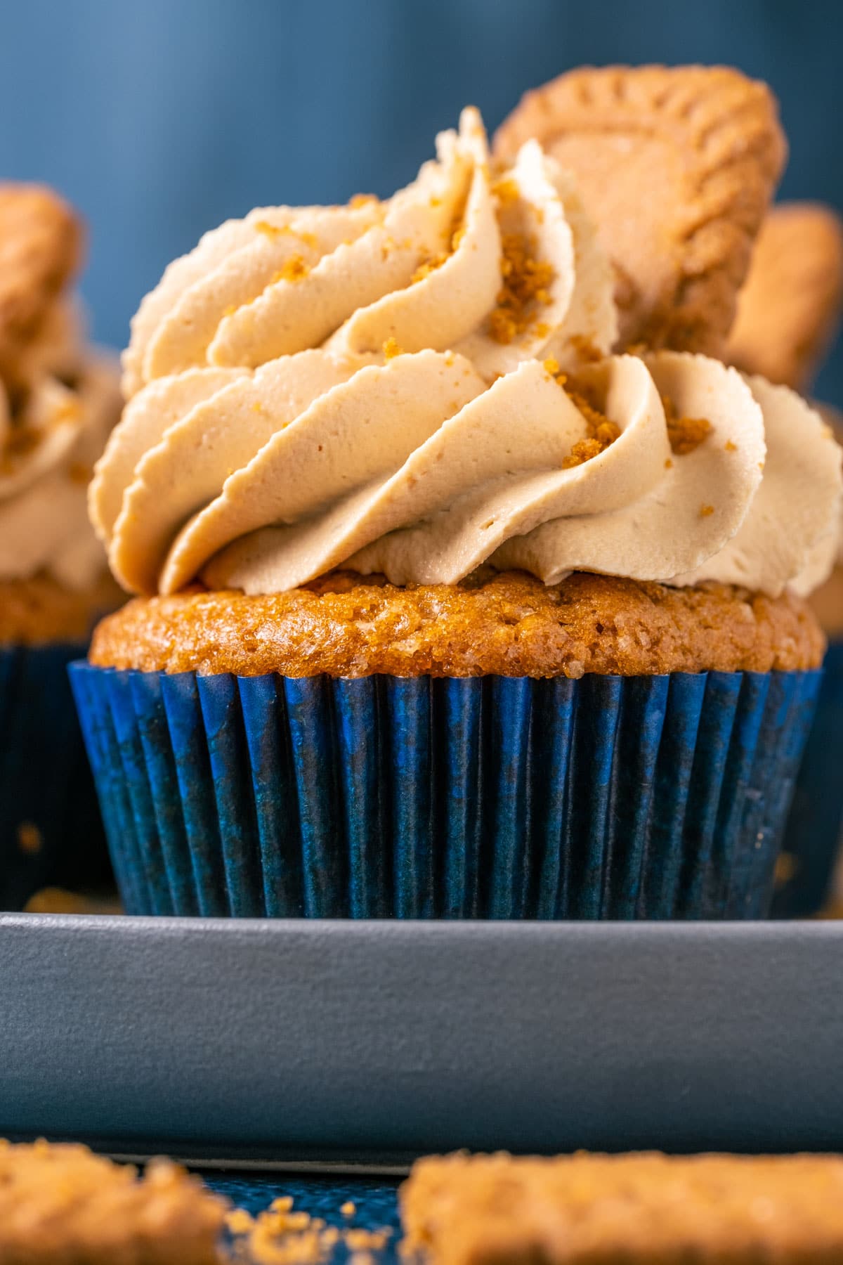 Vegan biscoff cupcakes topped with frosting and biscoff cookies on a gray plate.