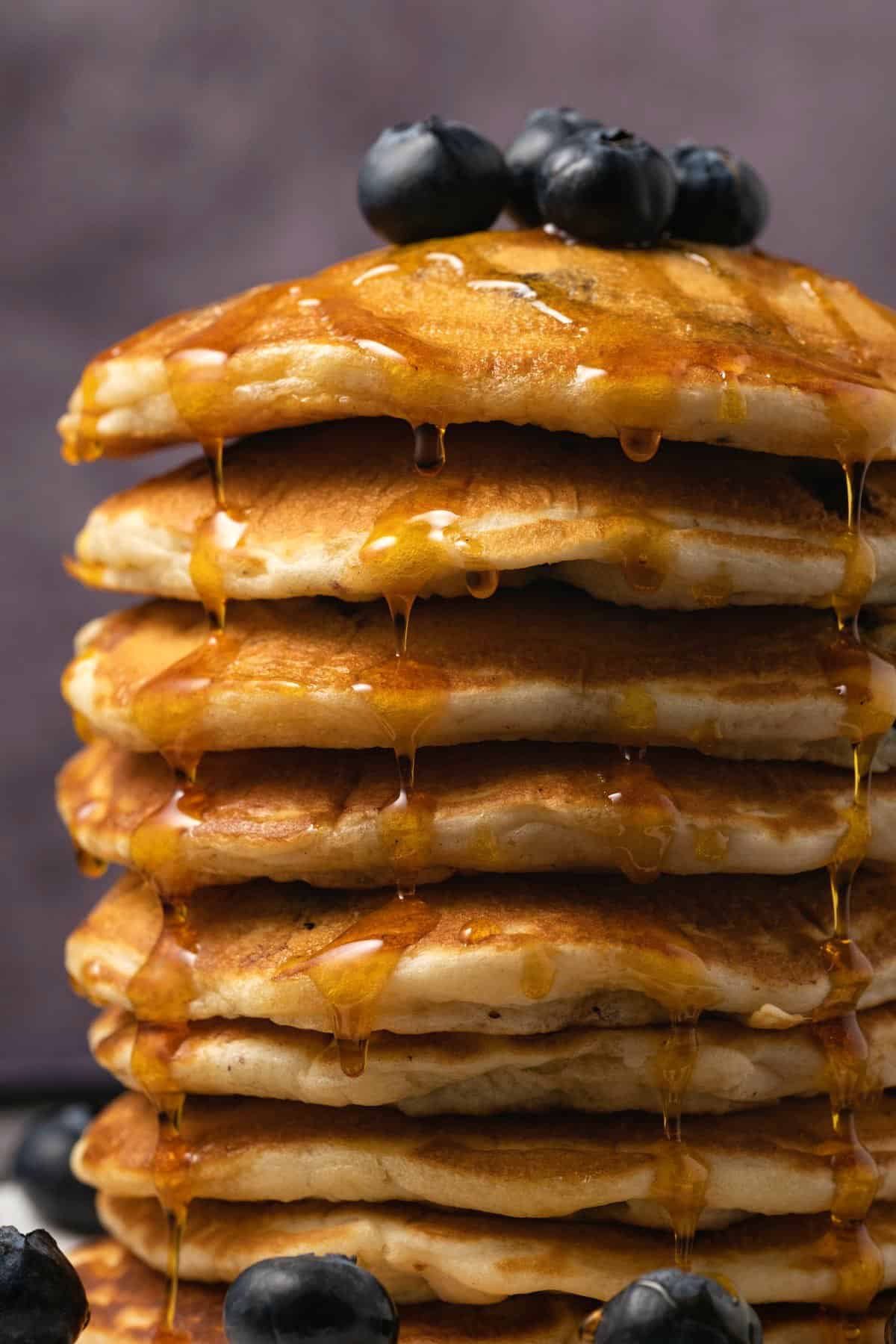 A stack of vegan blueberry pancakes with syrup and fresh blueberries. 