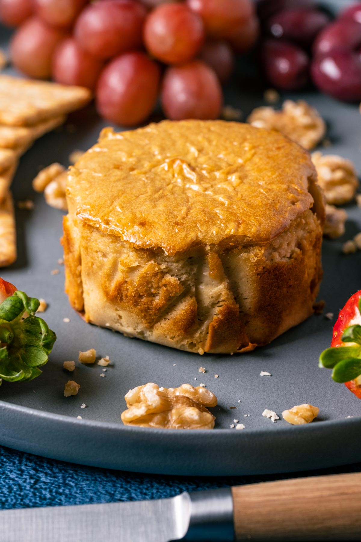 Circle of vegan brie cheese on a plate with fruits and nuts.