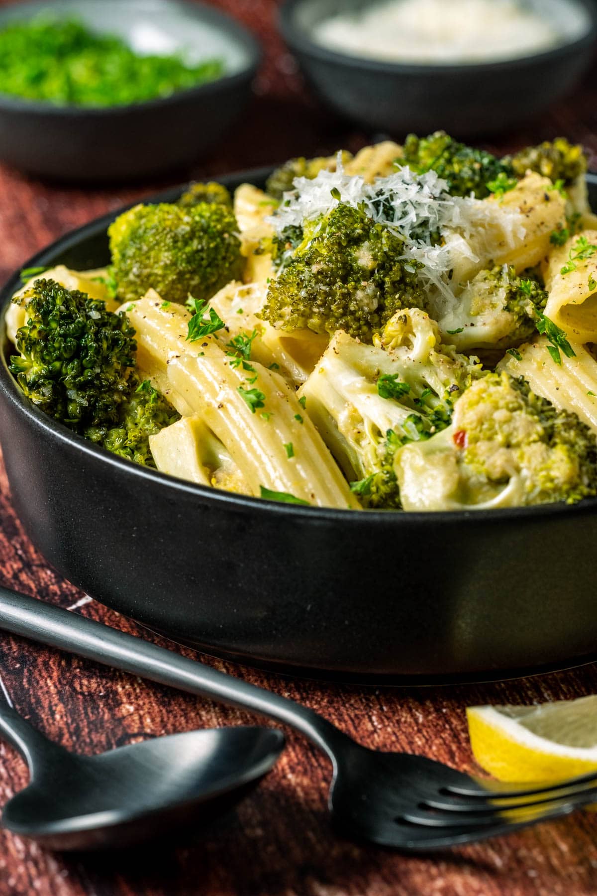 Vegan broccoli pasta topped with vegan parmesan in a black bowl.