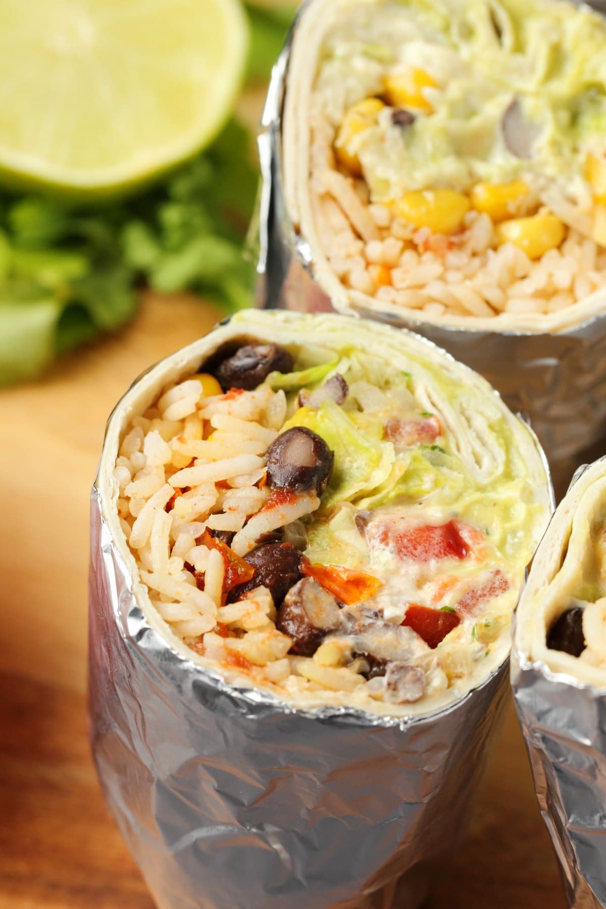 Vegan burritos cut in half and standing upright on a wooden cutting board. 