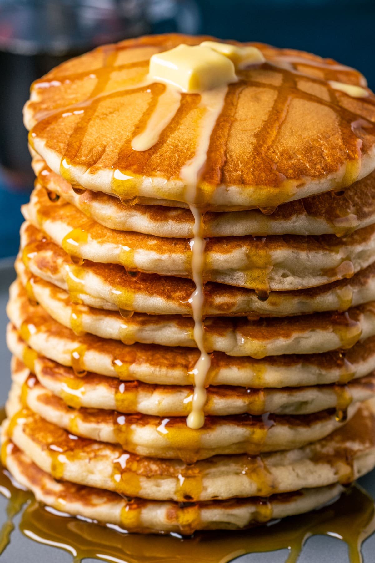 Stack of vegan buttermilk pancakes topped with vegan butter and syrup on a blue plate.