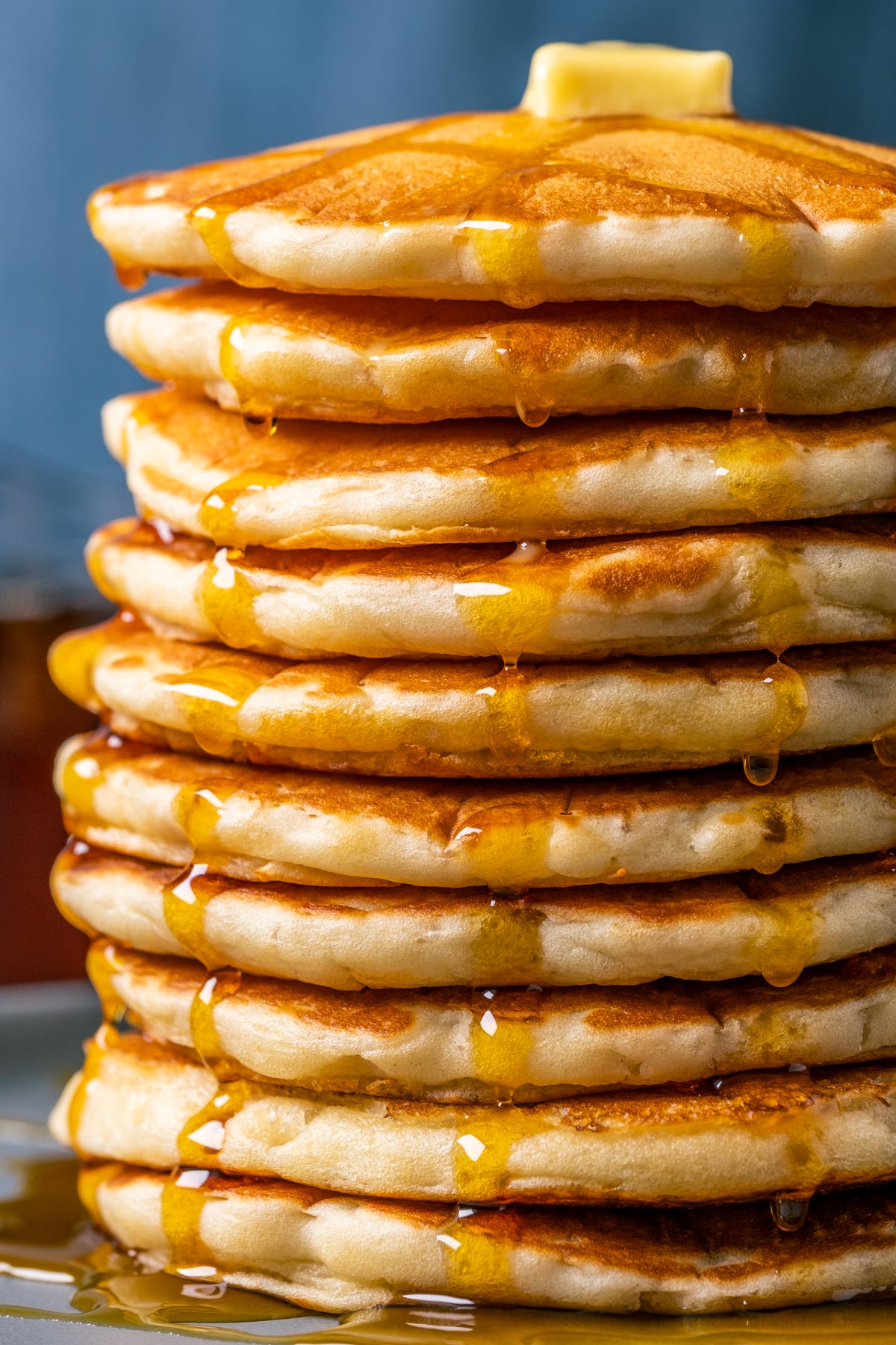 Stack of vegan buttermilk pancakes topped with vegan butter and syrup on a blue plate.