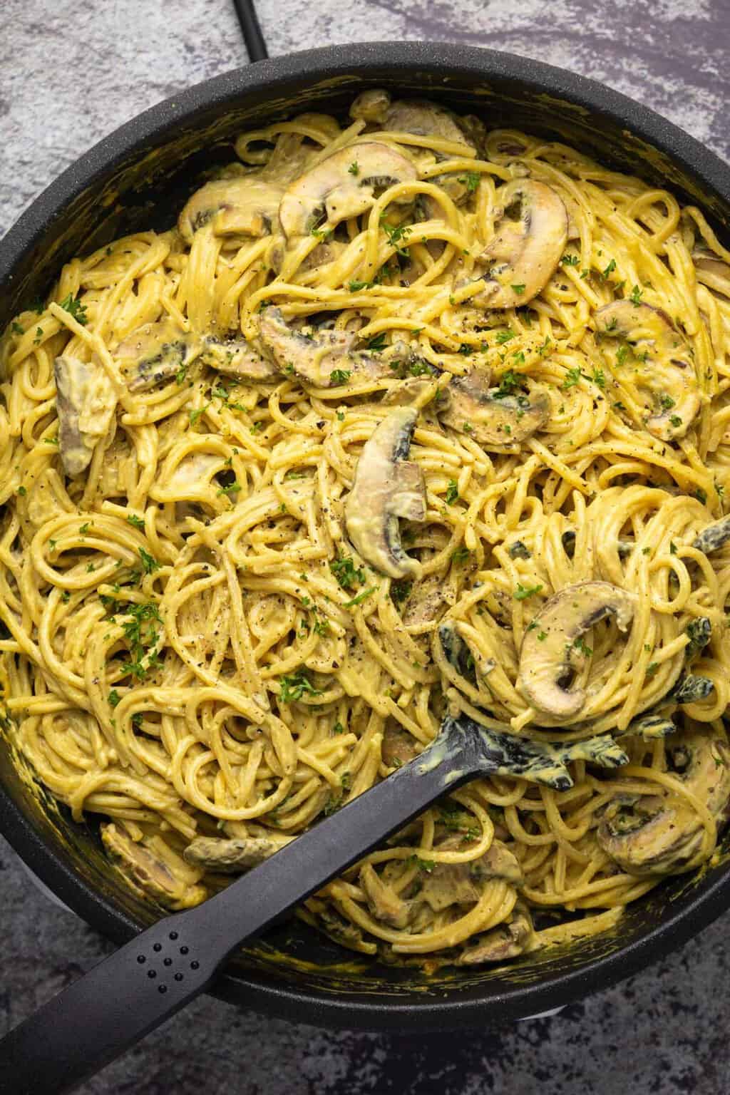 Vegan carbonara in a frying pan with a serving spoon. 