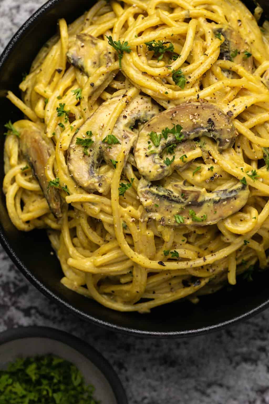 Vegan carbonara in a black bowl topped with chopped parsley. 