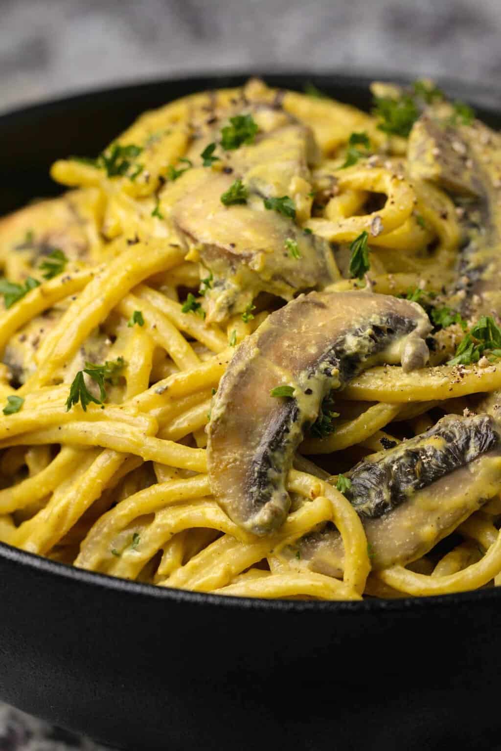 Vegan carbonara in a black bowl topped with chopped parsley.