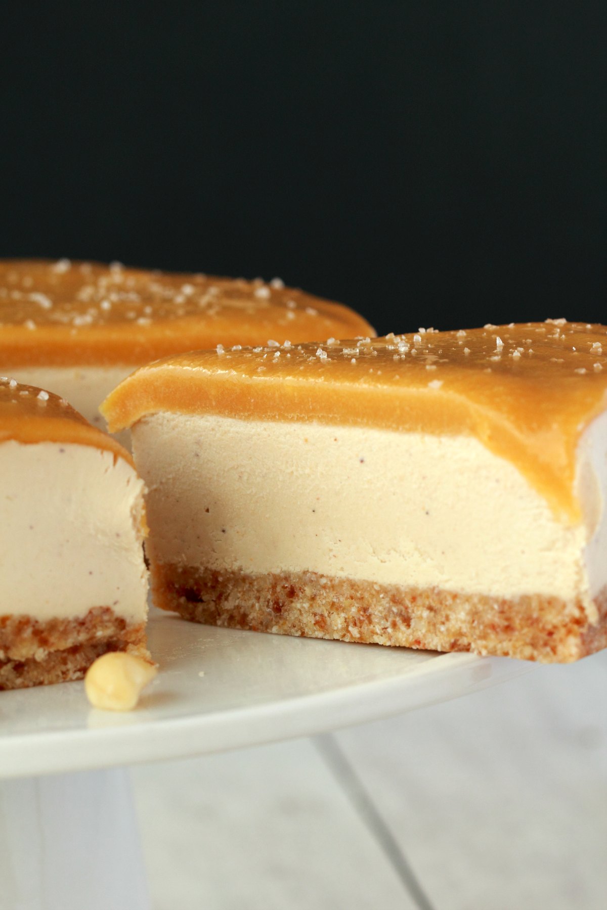 Vegan cheesecake with caramel fudge sauce on a white cake stand, with one slice halfway out. 