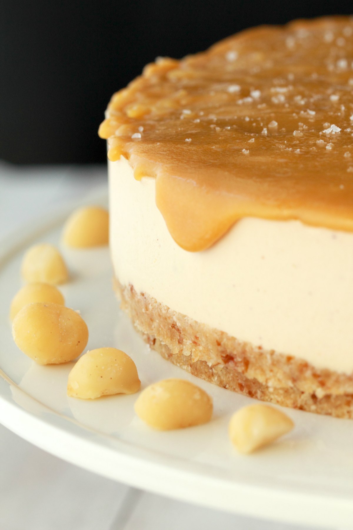 Vegan cheesecake and macadamia nuts on a white cake stand.