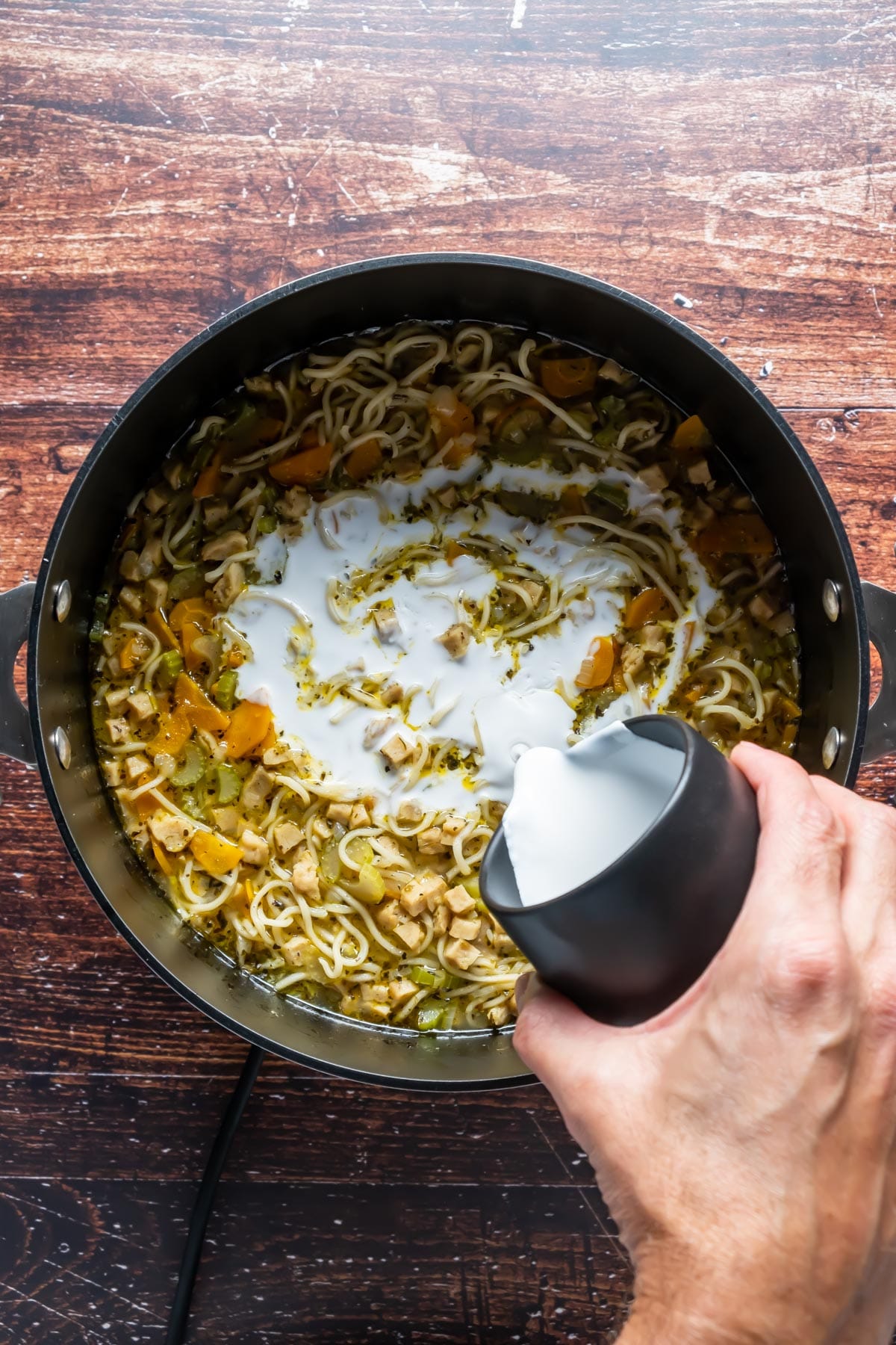 Adding coconut cream to a pot of vegan chicken noodle soup.