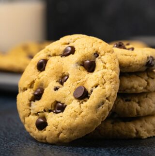 Vegan chocolate chip cookie leaning against a stack of cookies.