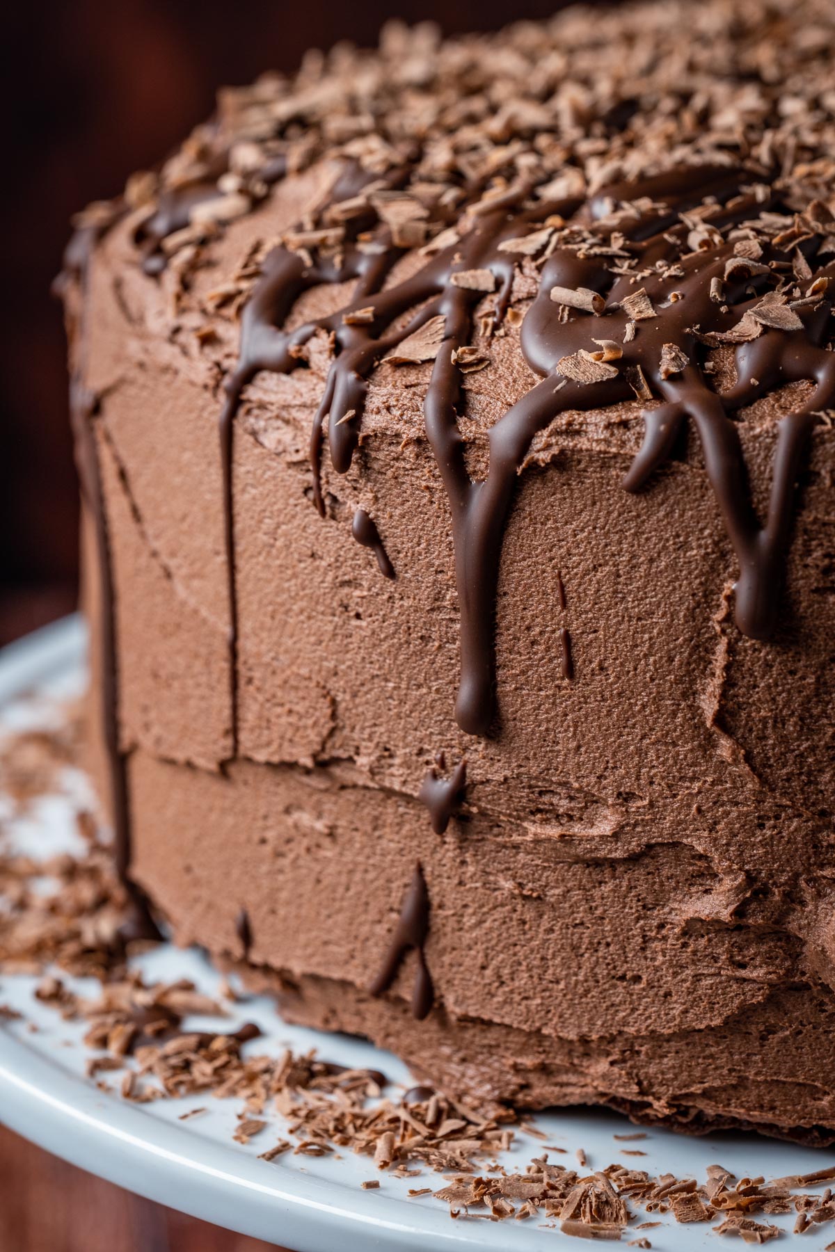 Vegan chocolate fudge cake on a white cake stand.