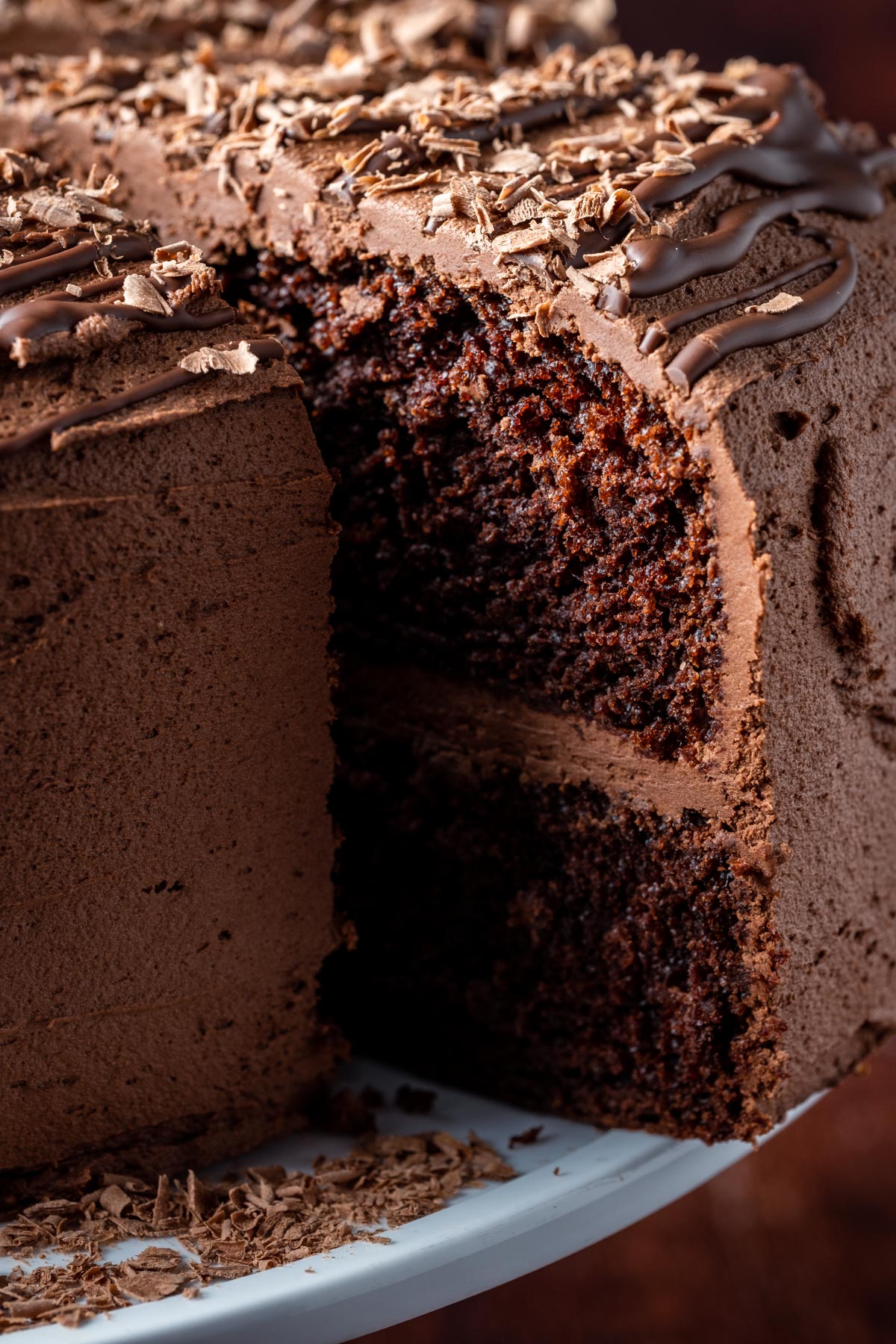 Sliced vegan chocolate fudge cake on a white cake stand. 