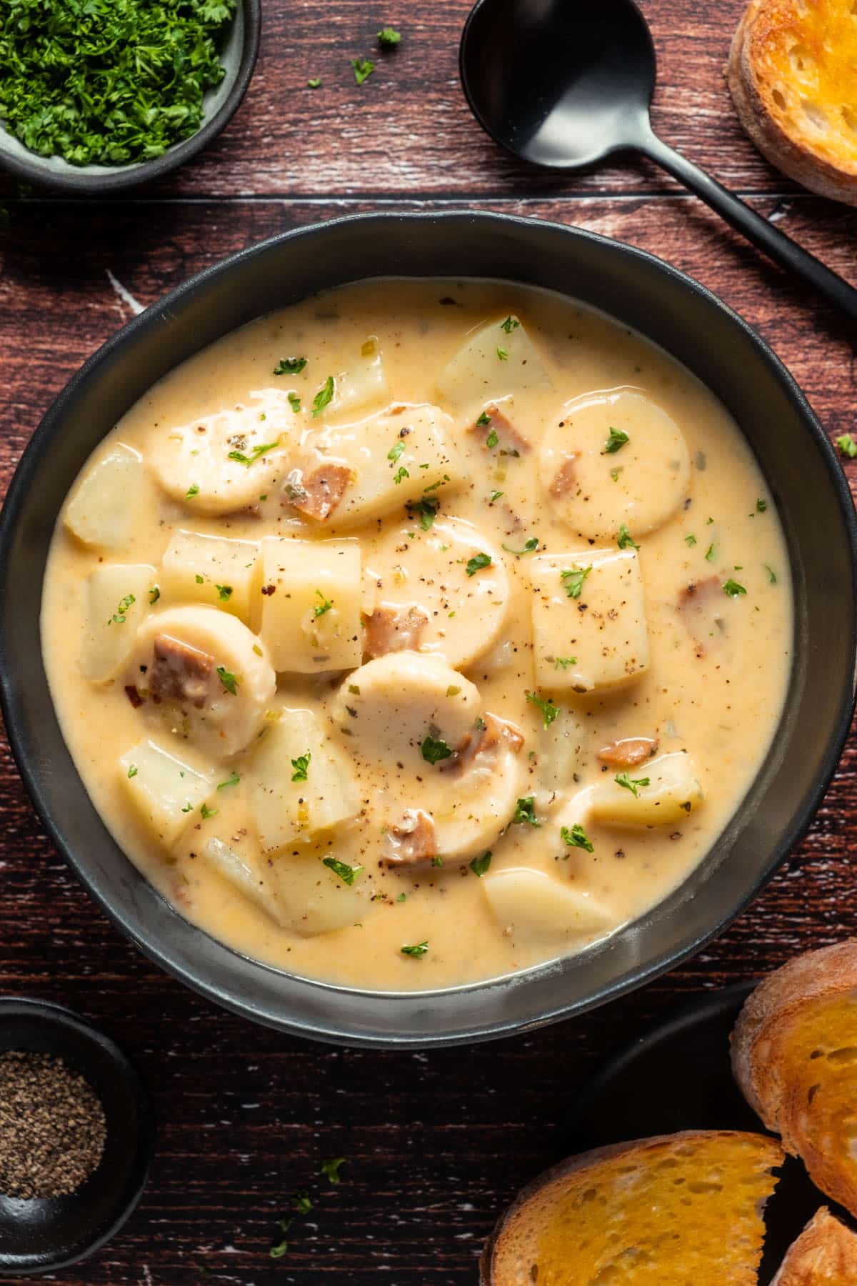 Vegan clam chowder topped with fresh chopped parsley in a black bowl. 