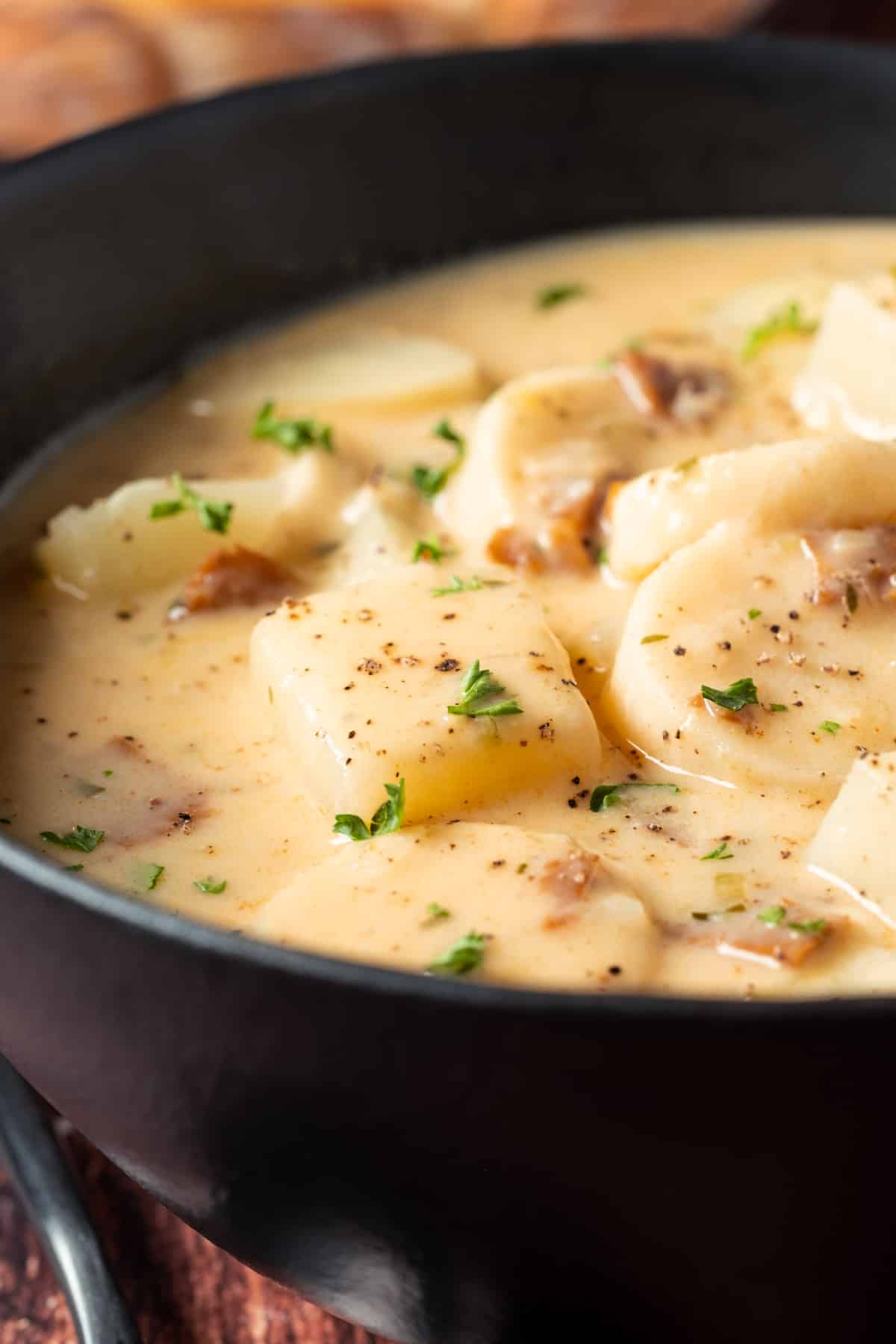 Vegan clam chowder topped with fresh chopped parsley in a black bowl.