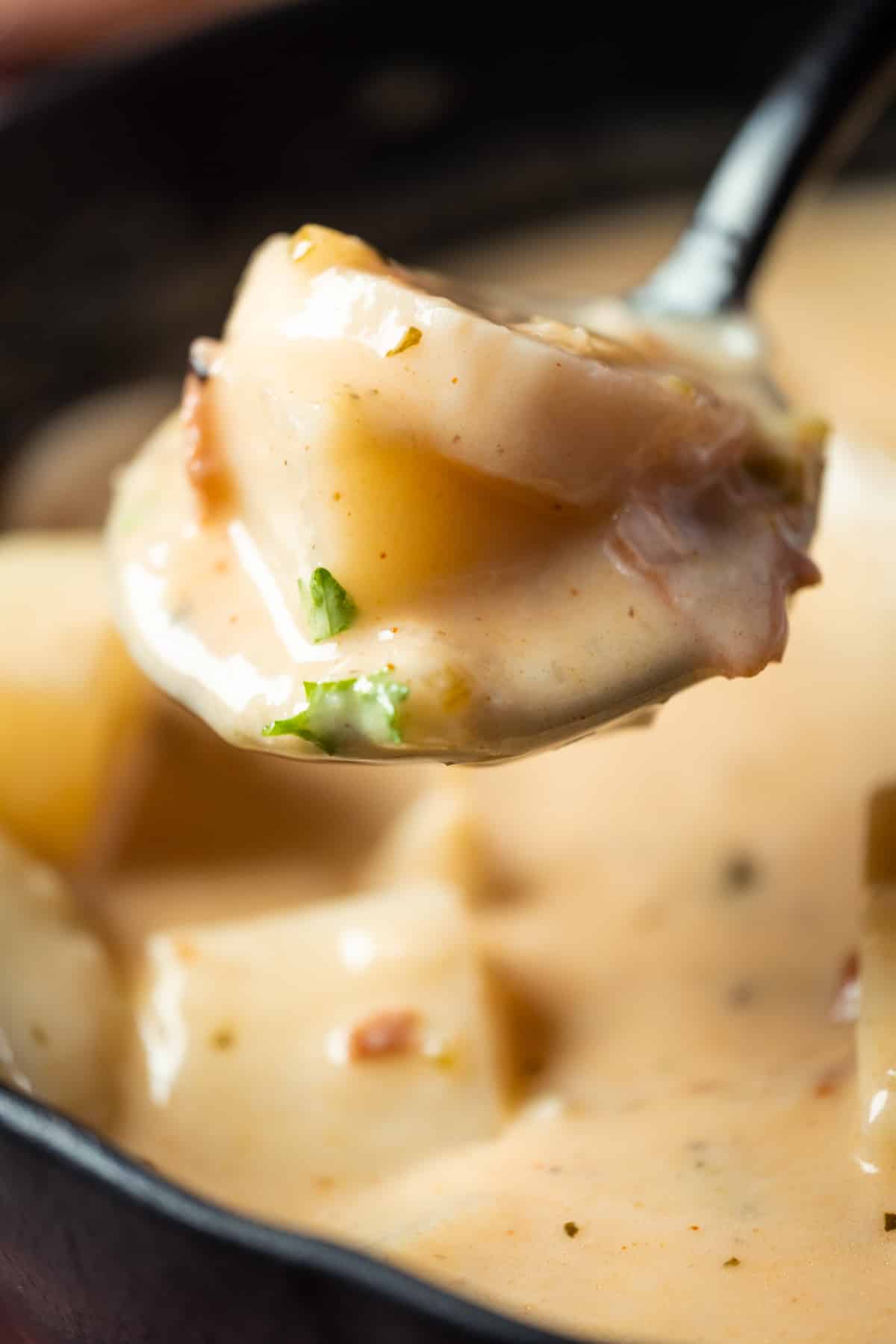 Vegan clam chowder topped with fresh chopped parsley in a black bowl with a spoon.