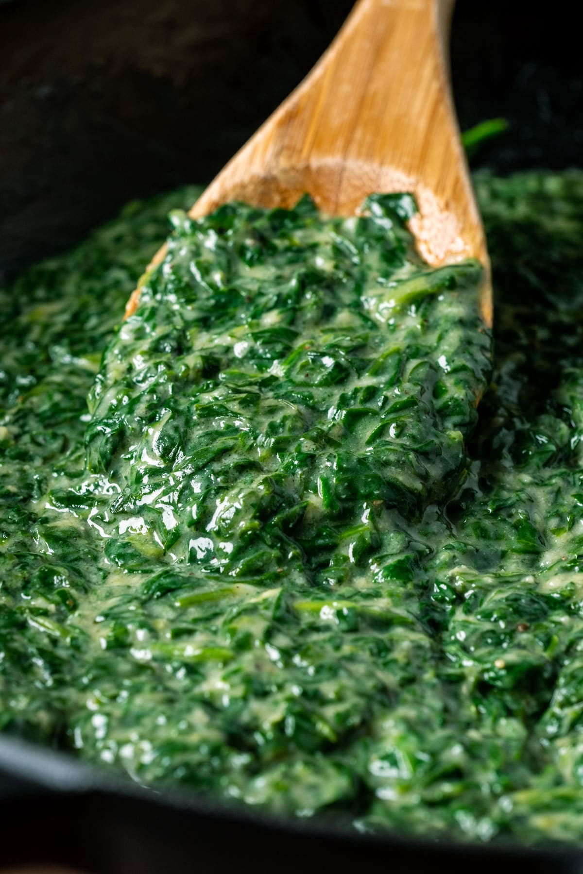 Vegan creamed spinach in a skillet with a wooden spoon.