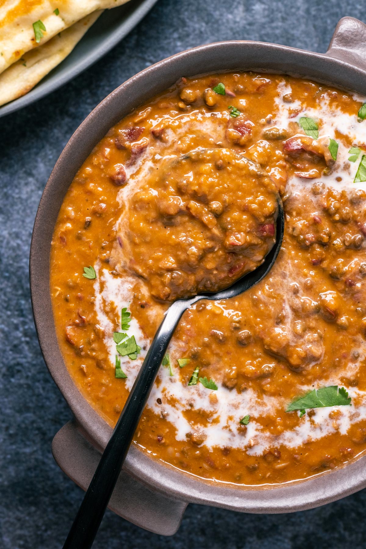 Vegan dal makhani topped with a drizzle of coconut cream and fresh chopped cilantro in a brown bowl with a spoon.