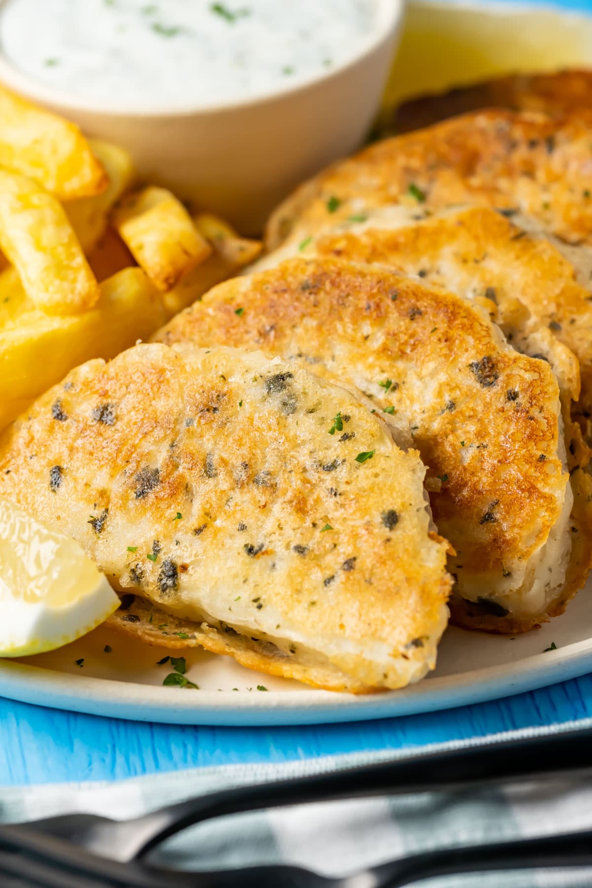 Beer battered vegan fish with chips, vegan tartar sauce and fresh lemon on a plate.