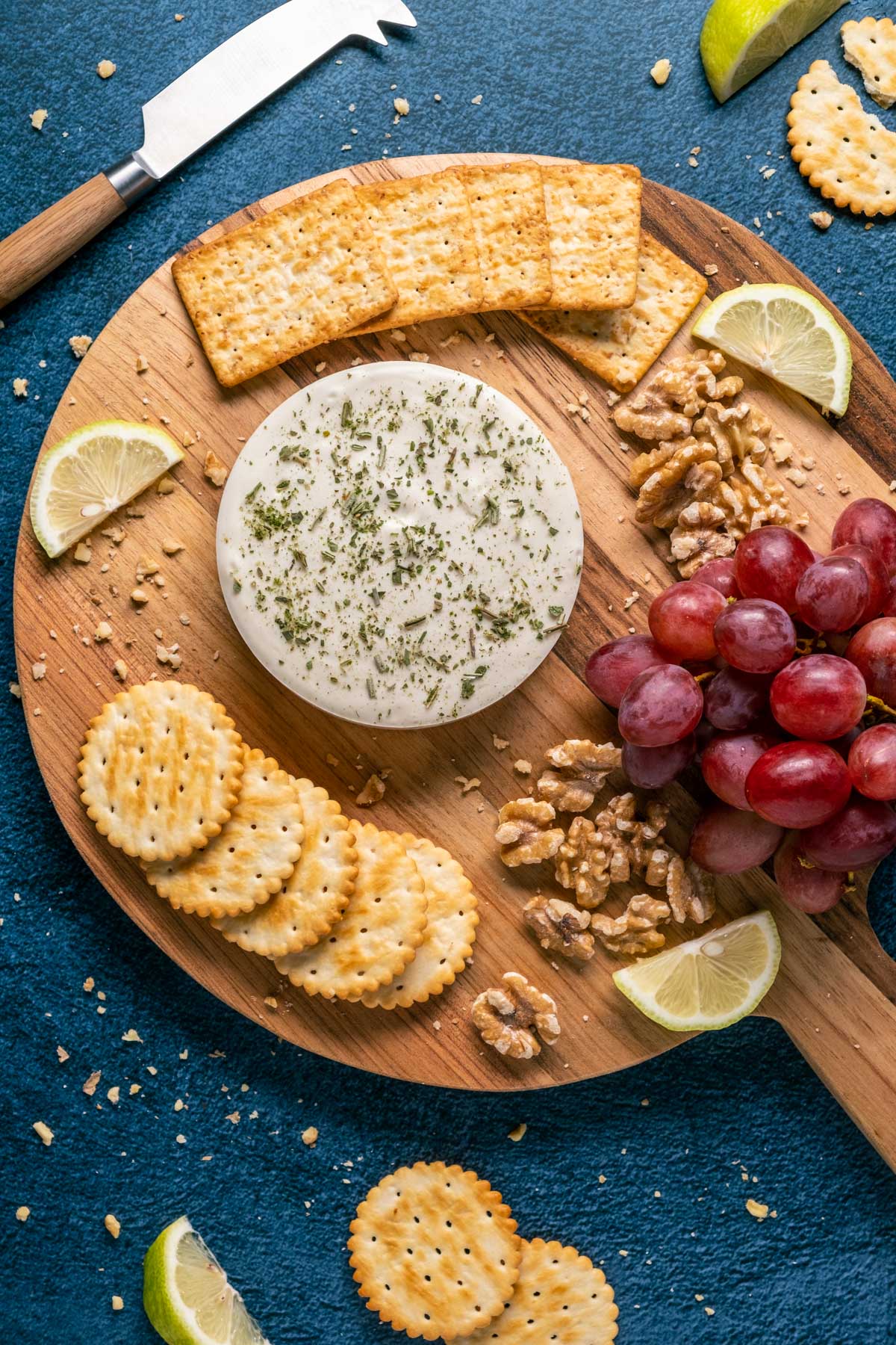 Vegan goat cheese on a wooden board with crackers, nuts and grapes.