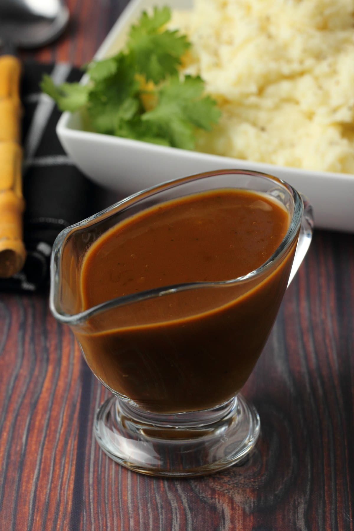 Vegan gravy in a glass gravy jug with mashed potatoes in the background. 