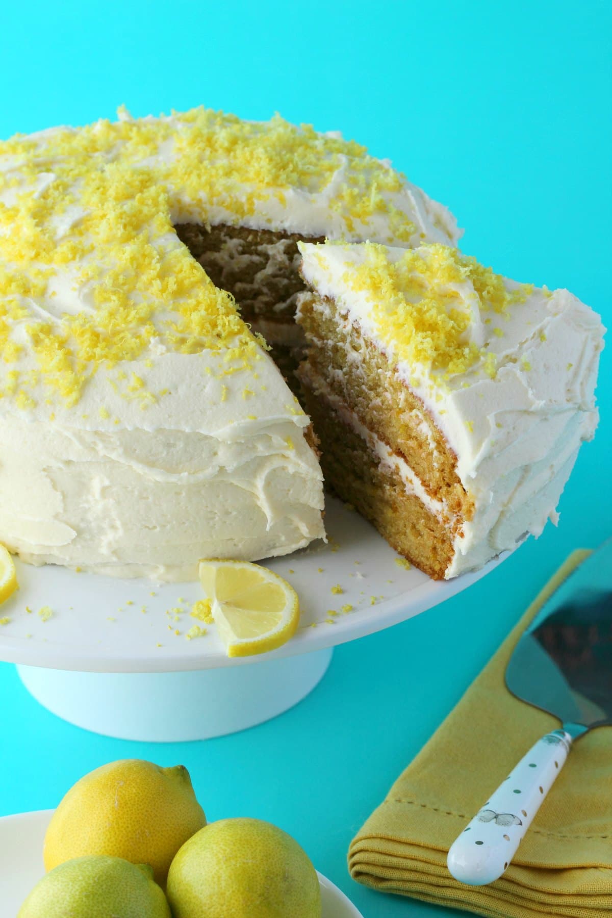 Lemon cake on a white cake stand, one slice cut and ready to be served. 