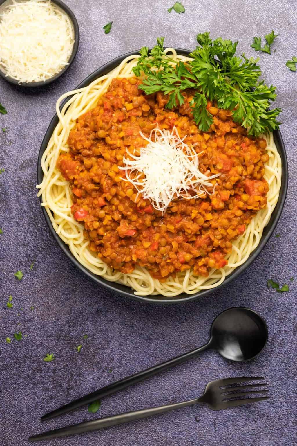 Lentil bolognese topped with vegan parmesan in a black bowl. 