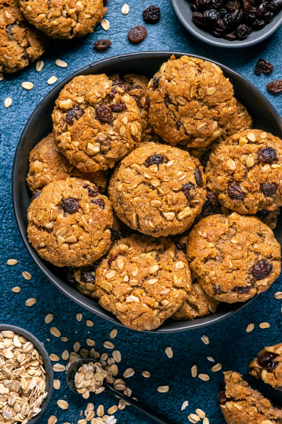 Vegan oatmeal raisin cookies stacked up on a black plate.