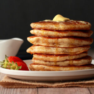 Vegan pancakes stacked up on a plate topped with vegan butter and syrup.